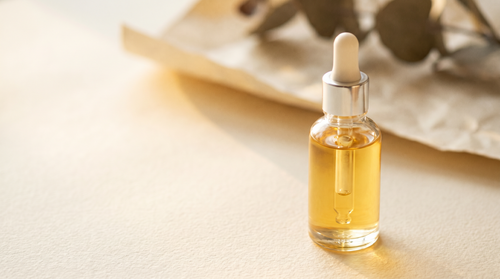 Clear glass dropper bottle of brightening serum in warm golden light.