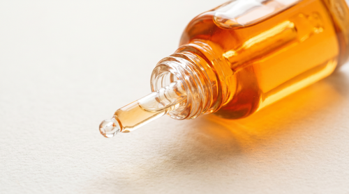 Clear glass dropper bottle of antioxidant serum in a warm citrus-toned light.